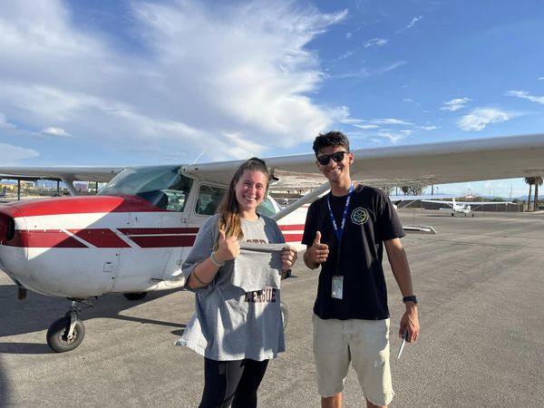 Student, in front of a plane, holding a cut shirt after her first solo flight