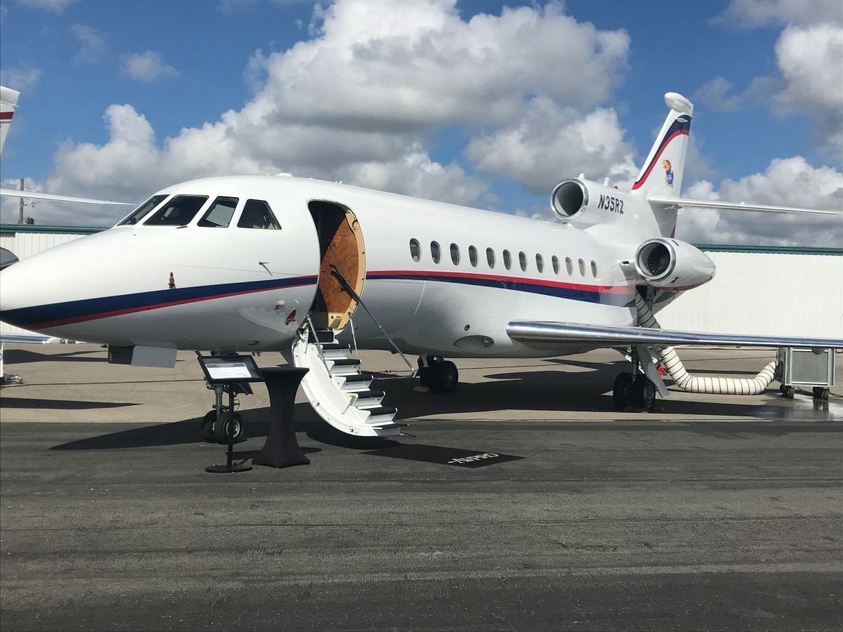 Private jet parked on airport ramp with stairway extended under partly cloudy sky.
